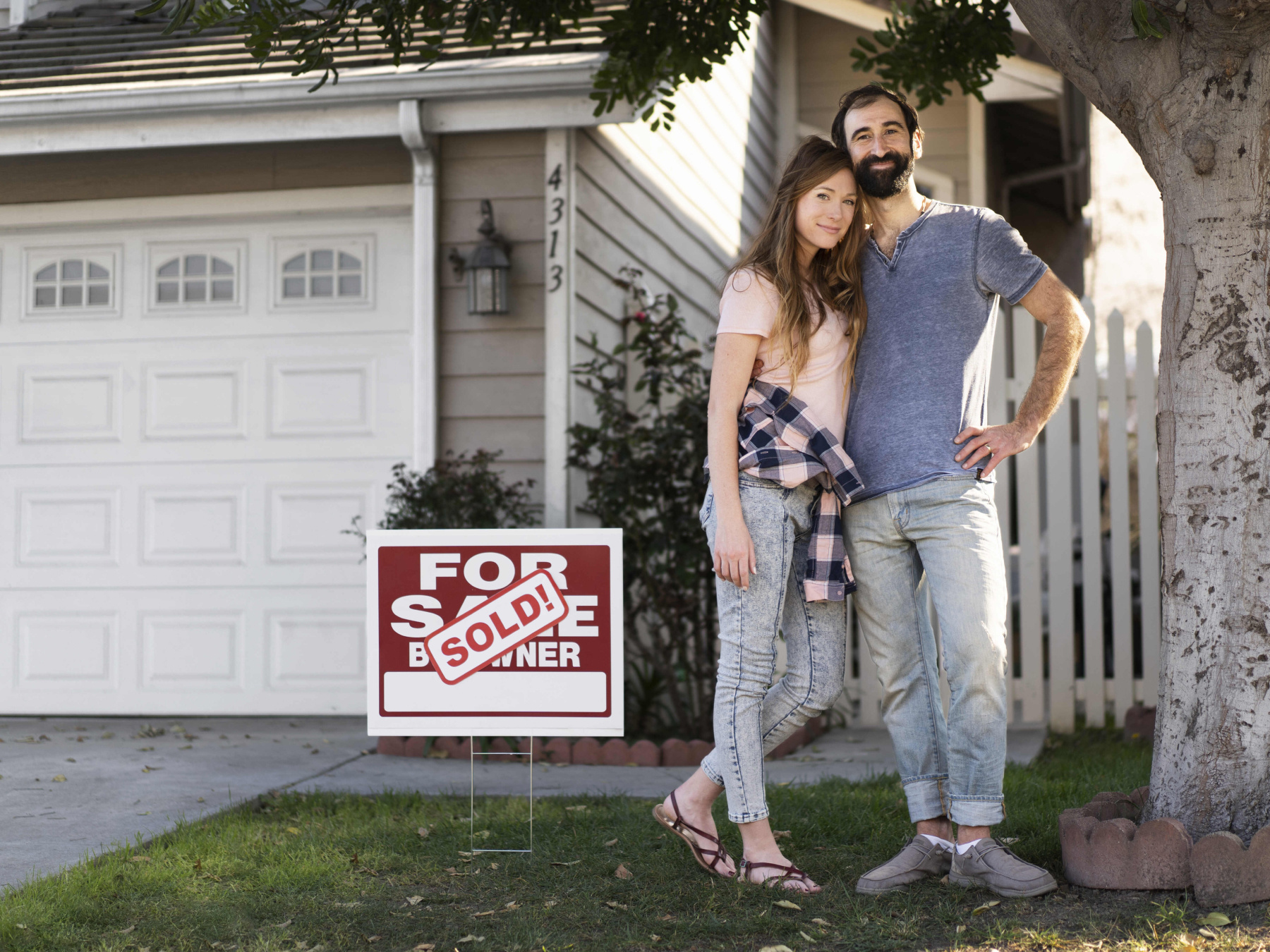 Homebuyer couple post in front of new home and for sale sign